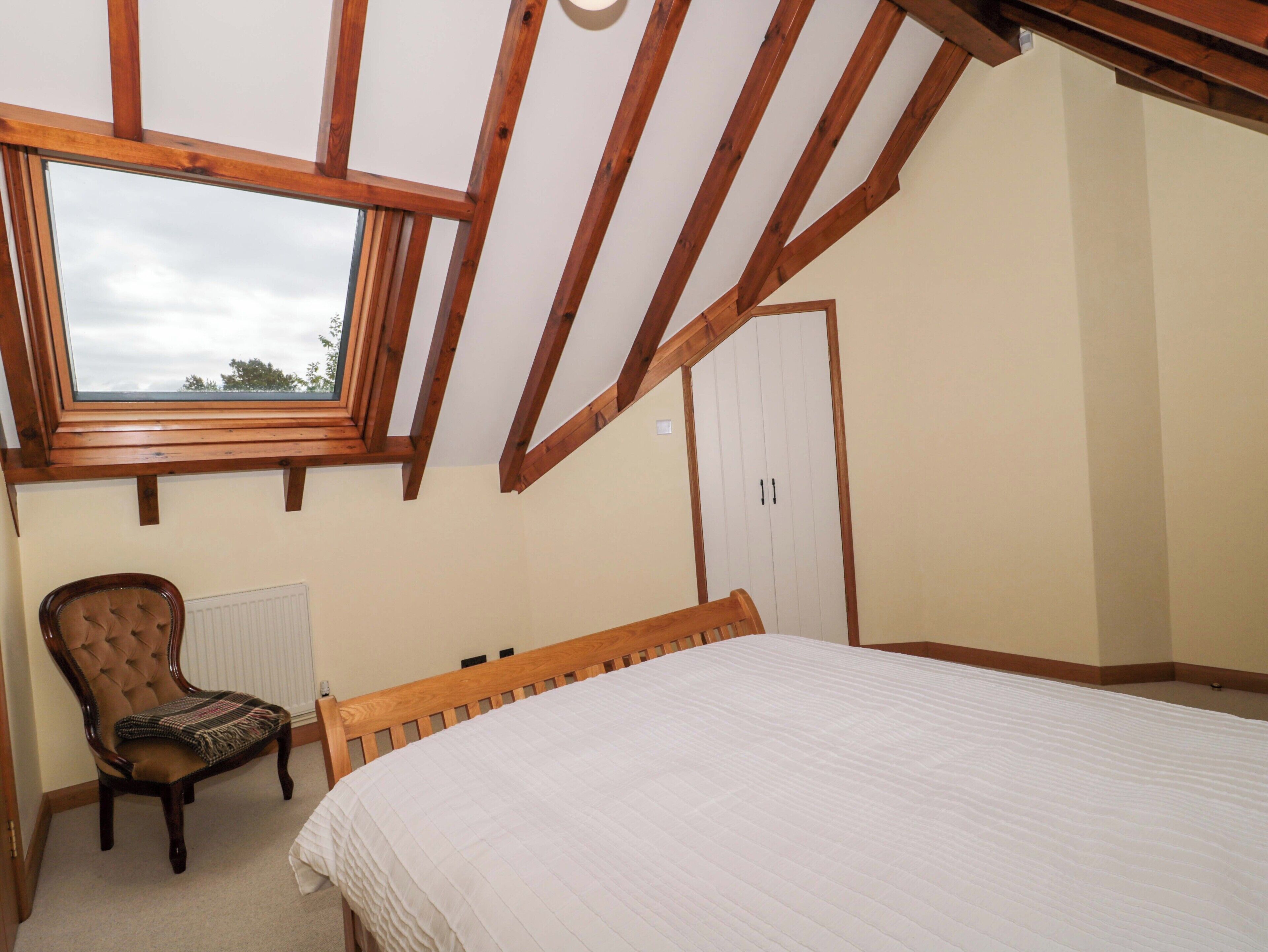 Une chambre avec un plafond en pente, une fenêtre, un lit, une chaise et une armoire.