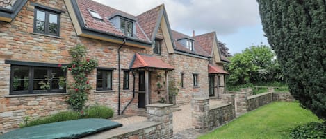 A stone house with a sloped roof, a small garden, and a tall tree.