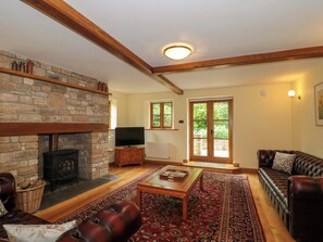 A living room with a stone fireplace, a television, a sofa, and a patterned rug. - Stowey Mead Stables (Bristol)