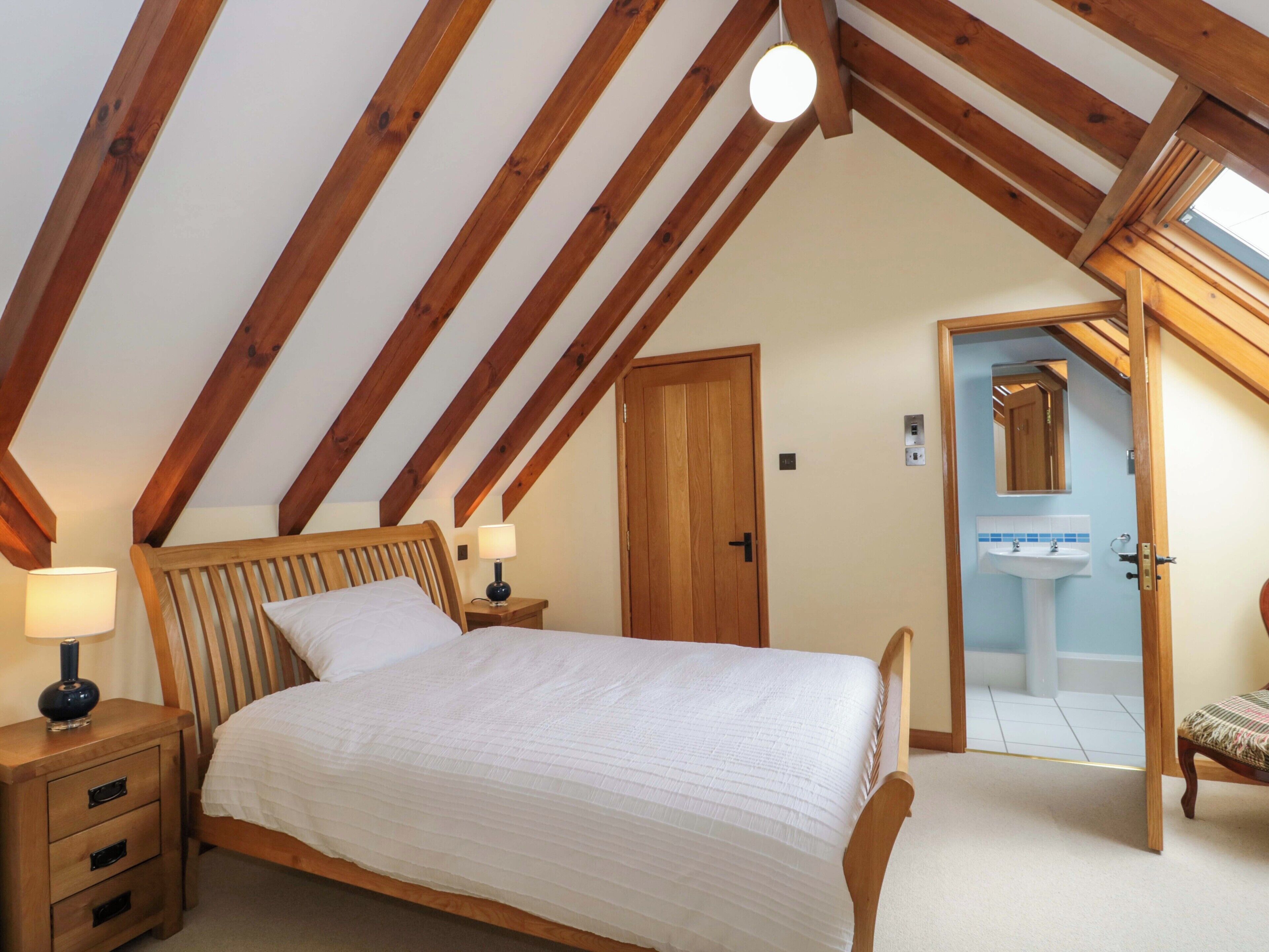 A bedroom with a wooden bed, nightstands, a lamp, a door, and a bathroom with a sink and mirror.