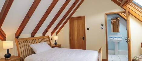 A bedroom with a wooden bed, nightstands, a lamp, a door, and a bathroom with a sink and mirror.