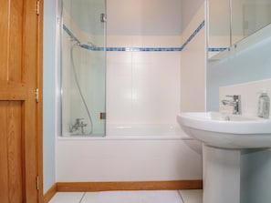 Ein Badezimmer mit Duschkabine aus Glas, einem weißen Waschbecken und einer Holztür.