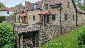Une maison en pierre avec un toit en pente, un porche à l’avant et un petit jardin.