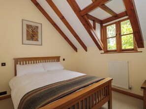 Ein Schlafzimmer mit einem hölzernen Bett, einem Fenster mit Ausblick, einem Heizkörper und einem gerahmten Bild an der Wand.