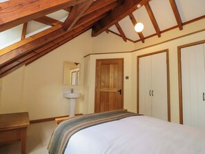 Ein Schlafzimmer mit geneigter Decke, Holzbalken, einem Bett, einem Nachttisch, einem Spiegel, einer Tür und einem Kleiderschrank.
