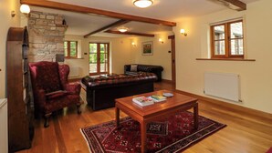 Un salon spacieux avec une cheminée en pierre, des poutres apparentes, un canapé en cuir, un fauteuil rouge et une table basse en bois.