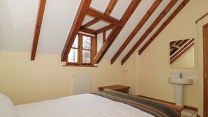 Une chambre avec un plafond en pente, une fenêtre, un radiateur, une table de chevet, un lit et une salle de bain avec un lavabo et un miroir.