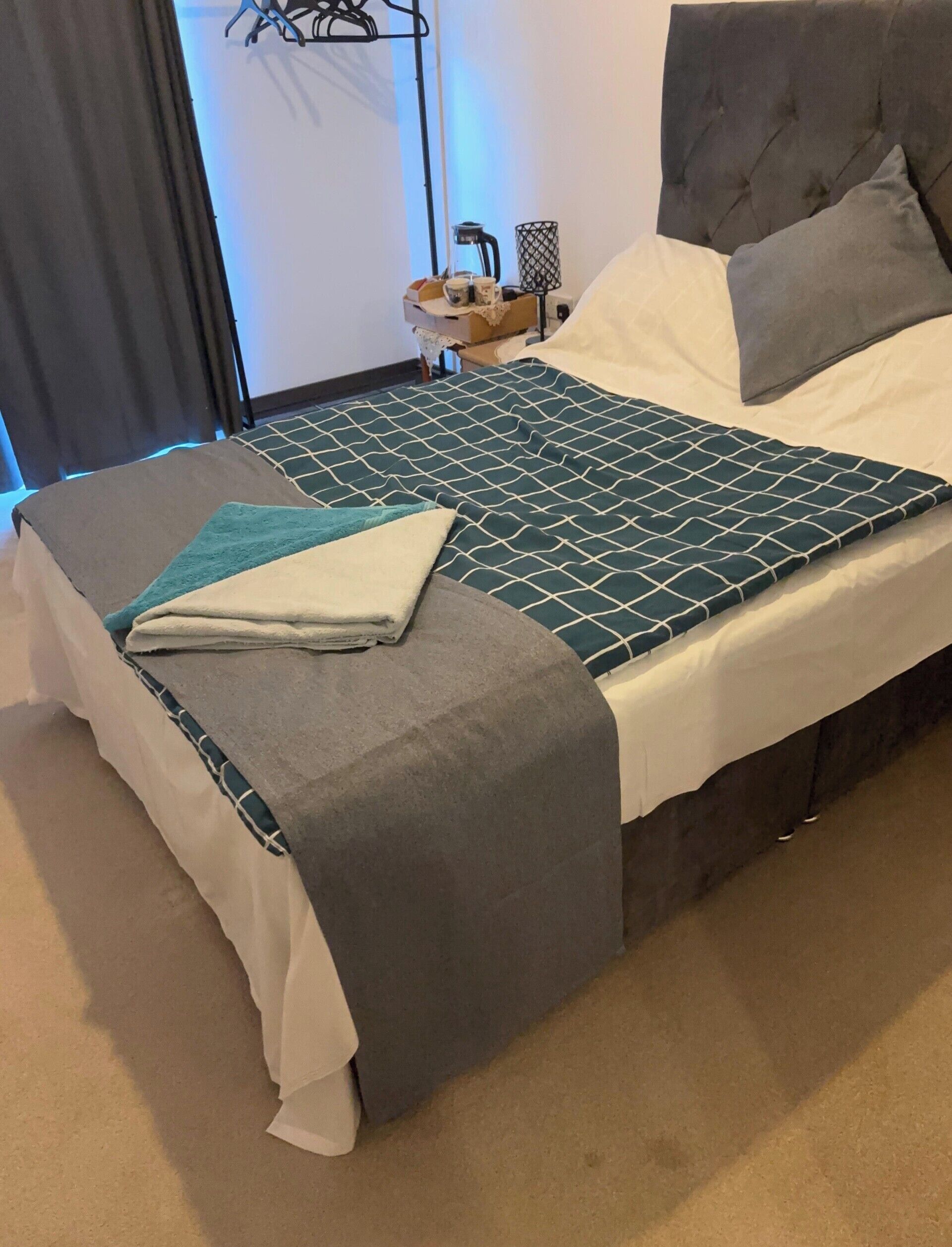 A neatly made bed with a patterned bedspread, a grey throw blanket, and a matching pillow.