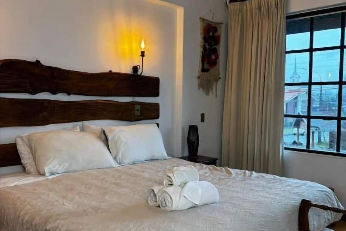 A hotel room with a large bed, a wooden headboard, a nightstand, and a window with curtains.