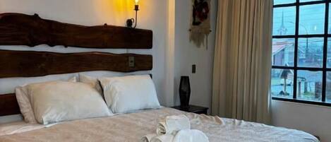 A hotel room with a large bed, a wooden headboard, a nightstand, and a window with curtains.