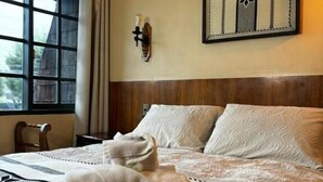 A hotel room with a bed, a window, a wall-mounted light fixture, and a framed artwork. - Hotel Boutique Wenupillan (Villarrica)