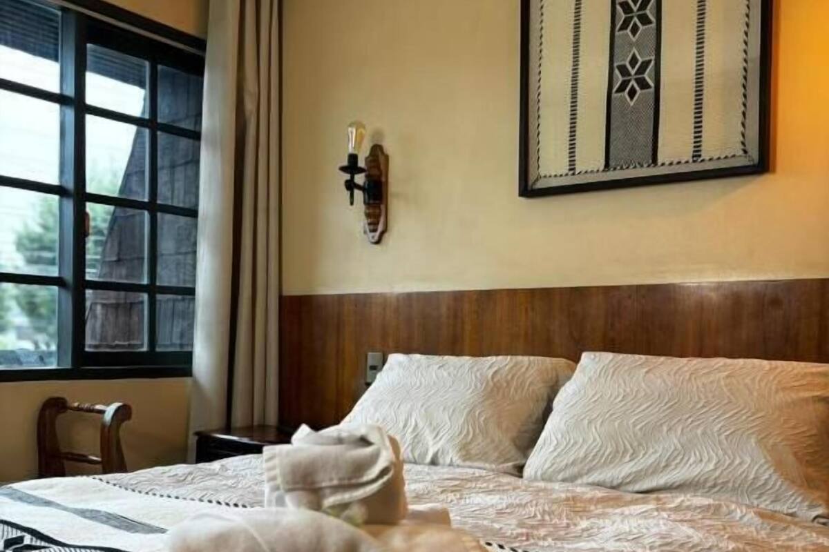 A hotel room with a bed, a window, a wall-mounted light fixture, and a framed artwork.