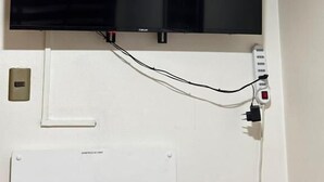 A flat-screen TV mounted on a wall with a power outlet and a thermostat below it. - Hotel Boutique Wenupillan (Villarrica)