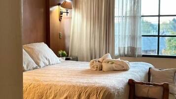 A hotel room with a bed, a chair, a window with curtains, and a lamp.