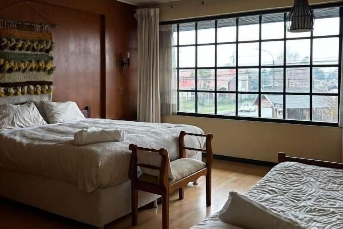 A bedroom with two beds, a wooden floor, a large window with a view, and a hanging tapestry.
