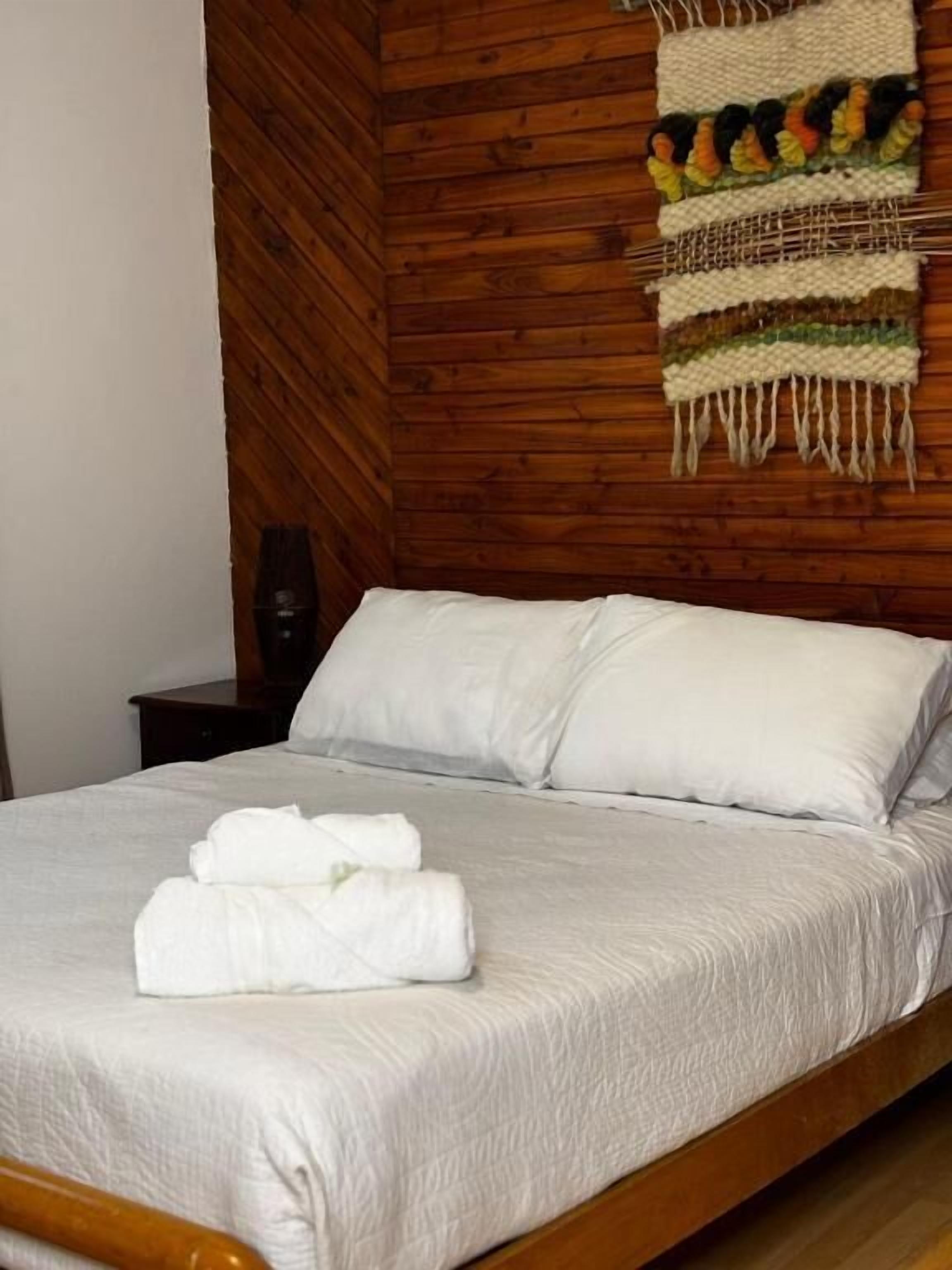 Cama com lençóis brancos, cabeceira de madeira e um objeto pendurado na parede.