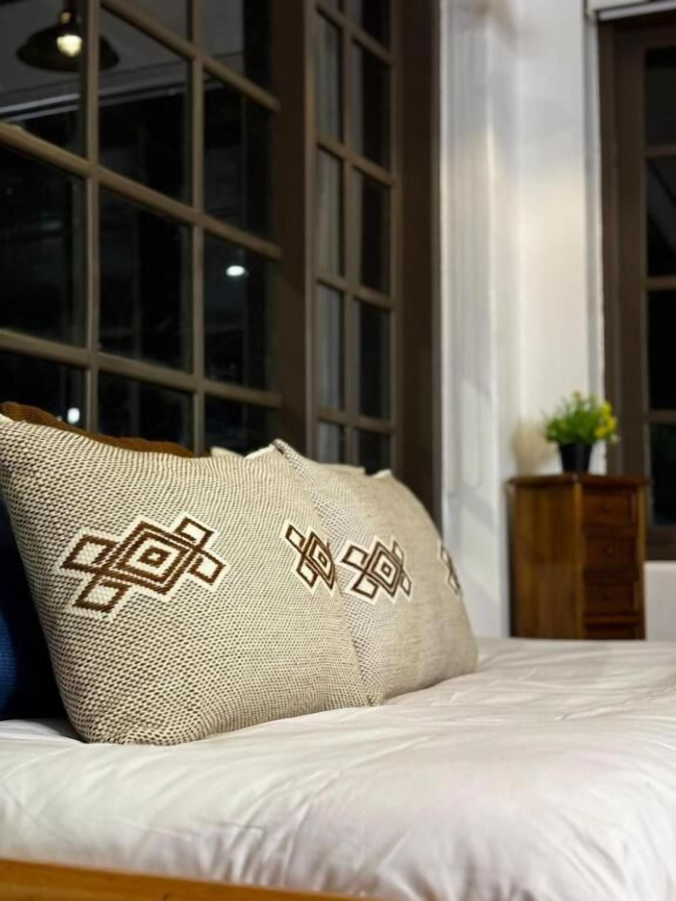 A bed with a patterned pillow and a wooden nightstand with a plant.