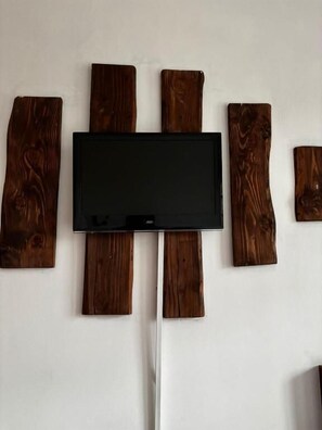 A flat-screen TV mounted on a wall with wooden planks arranged around it. - Hotel Boutique Wenupillan (Villarrica)