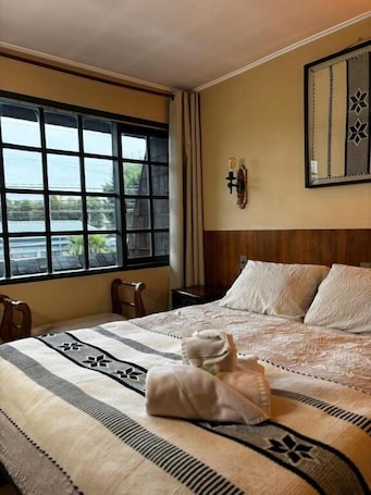 A hotel room with a large bed, a window with a view, a nightstand, and a wall-mounted lamp.. Hotel Boutique Wenupillan