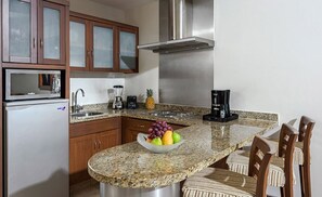 Uma cozinha com bancadas de granito, armários de madeira, eletrodomésticos de aço inoxidável e uma fruteira na ilha.