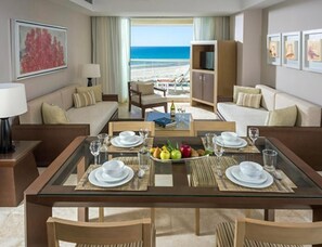 Ein Hotelzimmer mit Esstisch für vier Personen, einer Couch, einem Fernseher und Blick auf den Strand.