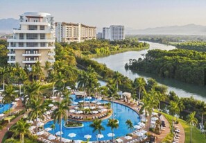 Et resort med en rund pool omgivet af palmer og liggestole, med bygninger i baggrunden.