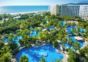 Et resort med flere swimmingpools omgivet af palmer, udsigt til en strand og en stor hotelbygning.