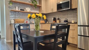 A modern kitchen with wooden cabinets, a stainless steel refrigerator, a microwave, and a dining table with chairs. - Phinney Ridge Comfy Digs! (Seattle)