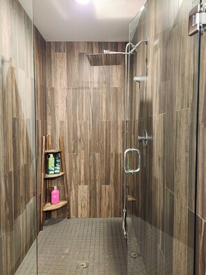 A shower with a glass door, a wooden shelf with toiletries, and a tiled floor. - Phinney Ridge Comfy Digs! (Seattle)