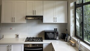 A modern kitchen with white cabinets, a gas stove, an oven, a microwave, and a window with a view of greenery. - Luxury 2-bedroom apartment in Victoria Falls near the falls (Victoria Falls)