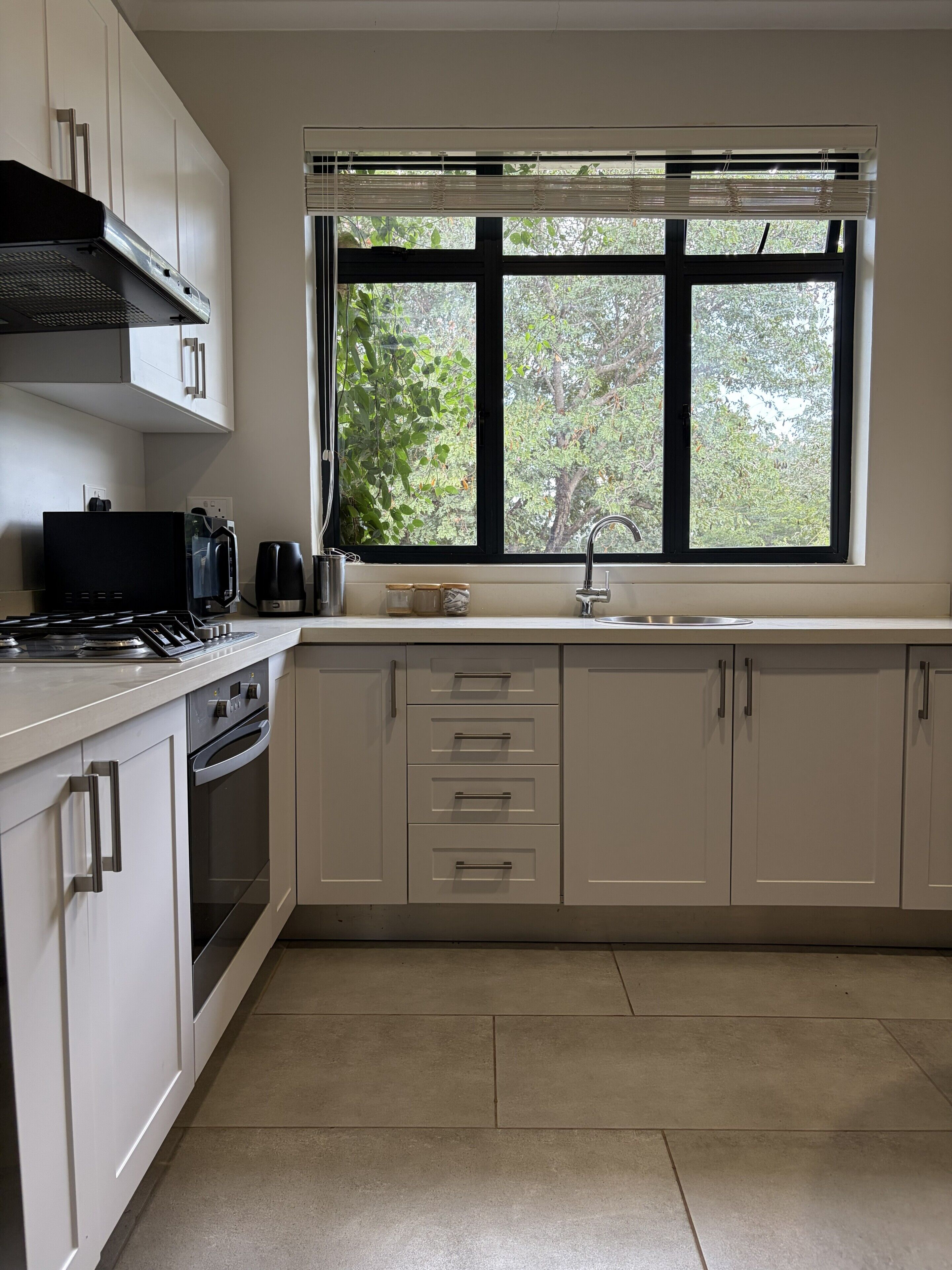 A modern kitchen with a stove, oven, sink, and window overlooking greenery.