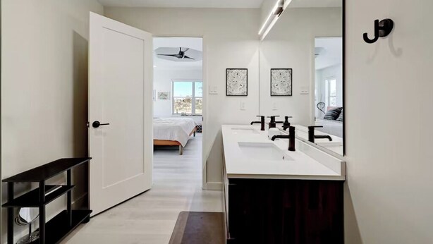 Un baño moderno con un espejo grande, dos lavamanos y un ventilador de techo.