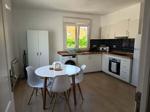A compact kitchen with a dining area, a washing machine, and a view through the window.