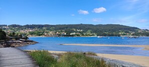 A coastal scene with a wooden pier, sandy beach, and boats on the water. - Vrbo Property (Cangas)