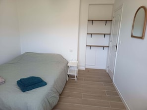 Une chambre à coucher comprenant un lit, une petite table de chevet, un miroir et une armoire avec des étagères.