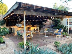An outdoor patio with a wooden pergola, string lights, and seating arrangements. - Mid-century house in South Redlands with shady backyard, treehouse and pergola (Redlands)