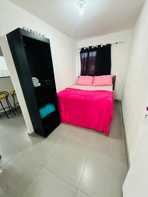 A small, compact room with a bed, a black wardrobe, and a small table with chairs. - Vrbo Property (São Paulo)
