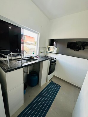 A compact kitchen with a sink, microwave, gas stove, and a window. - Vrbo Property (São Paulo)