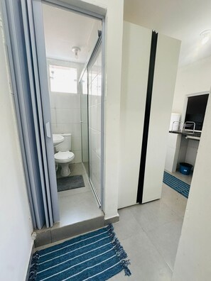 A bathroom with a toilet, shower, and a small shelf with toiletries. - Vrbo Property (São Paulo)