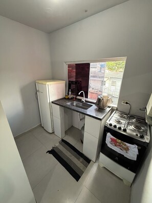 A compact kitchen with a refrigerator, sink, stove, and a window providing natural light. - Comfortable Furnished Apartment in the North Zone of São Paulo (São Paulo)
