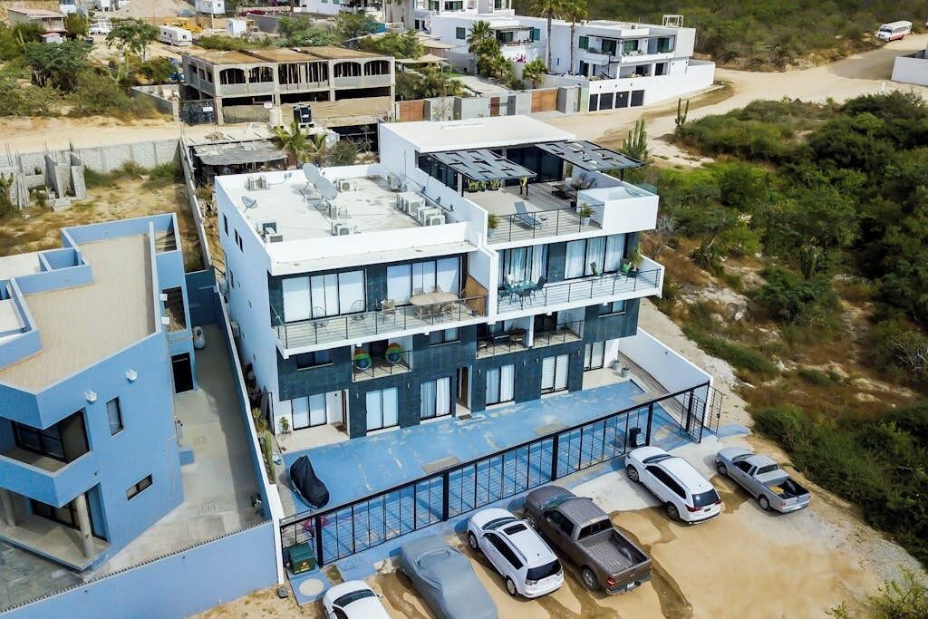 Um edifício com vários andares, um terraço no telhado, uma piscina e uma área de estacionamento com vários carros.