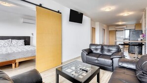 Una sala de estar moderna con un sofá, una mesa de centro de vidrio, una cama y un televisor montado en la pared.