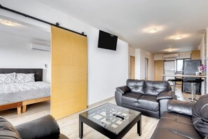A modern living room with a sofa, a glass coffee table, a bed, and a TV mounted on the wall. - Ocean View Condo With Scenic Balcony, Well-equipped Kitchen, Internet & W/D (Cabo San Lucas)