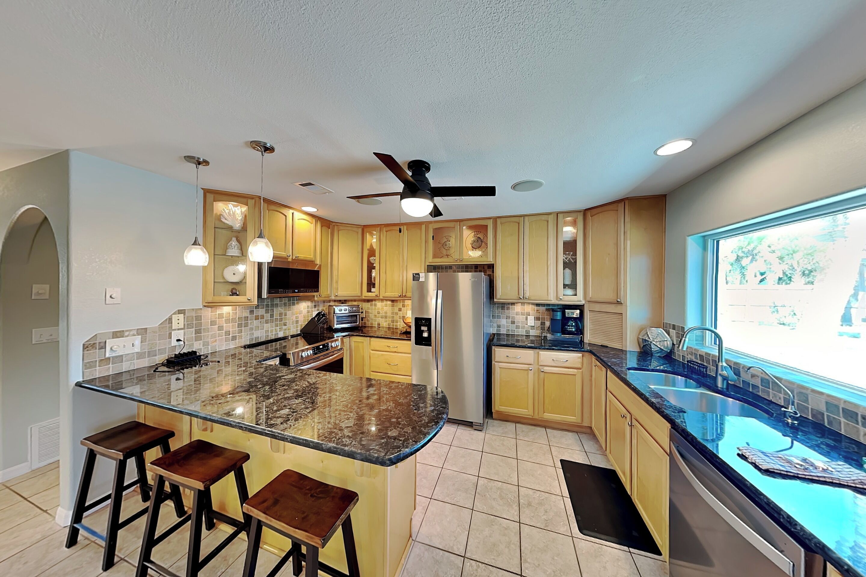Una cocina moderna con una isla central, taburetes de bar, un refrigerador y una ventana con vistas.
