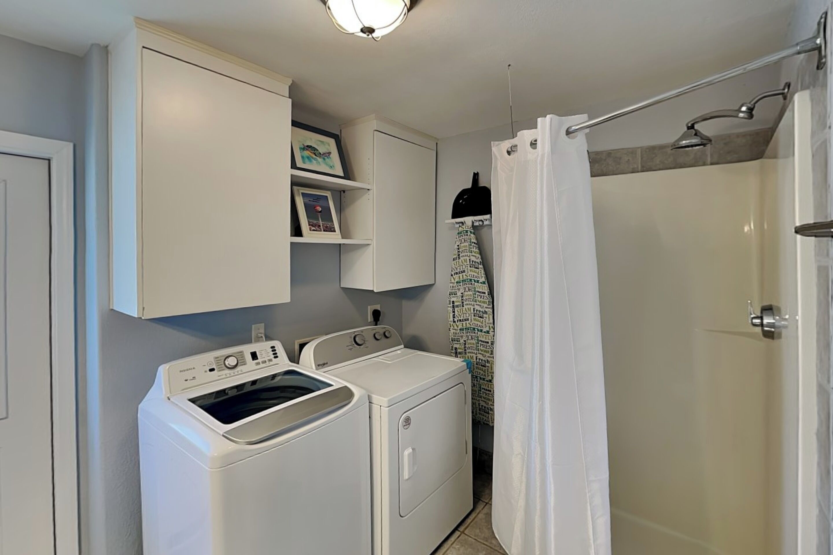 A laundry room with a washing machine, dryer, and a shower area.