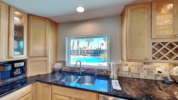 Una cocina con armarios de madera, un lavamanos doble, una cafetera y vistas a una piscina.