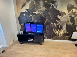 Un téléviseur à écran plat, posé sur un support noir, avec un papier peint à motifs floraux en arrière-plan.