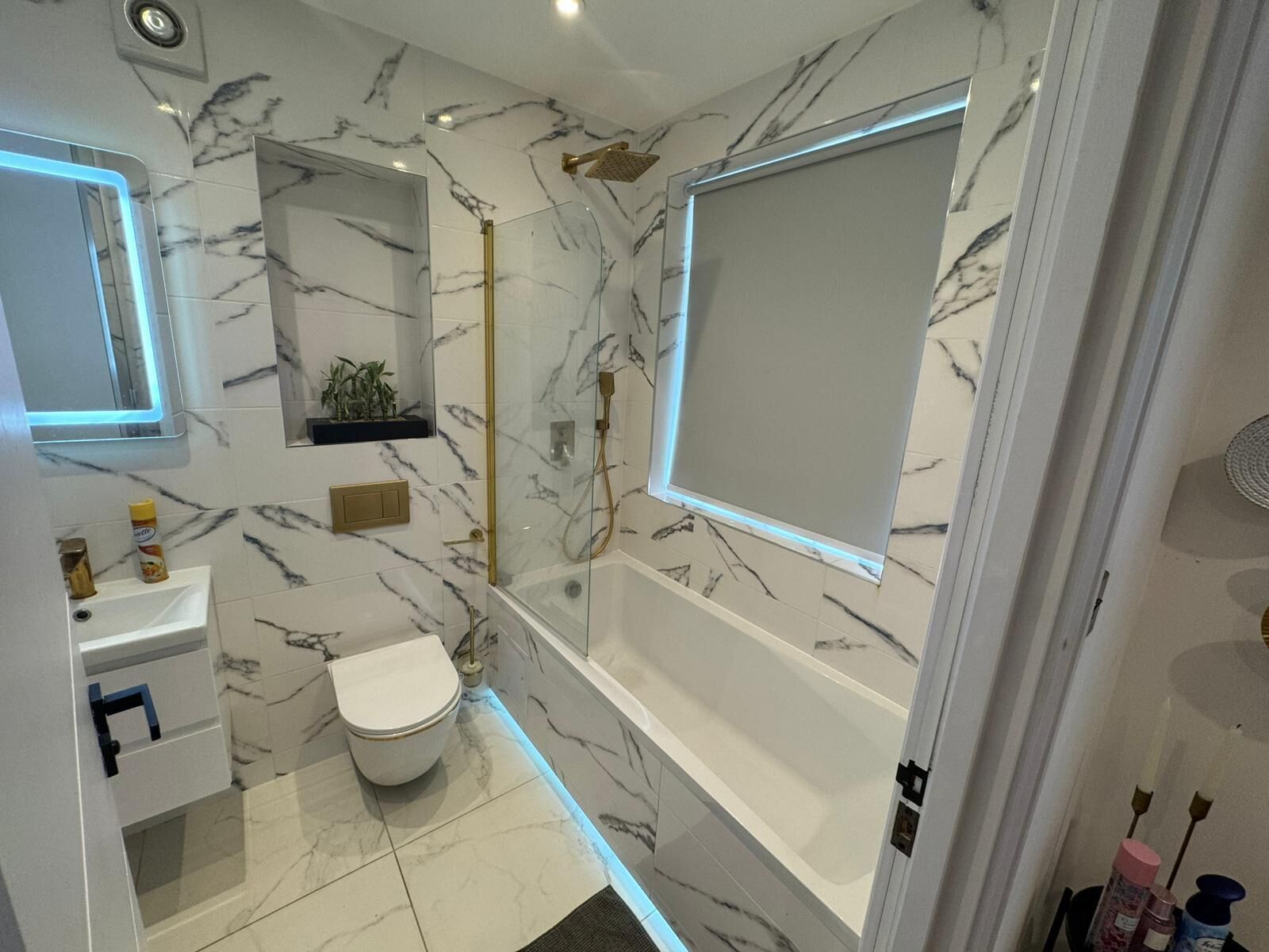 Une salle de bain moderne avec un sol en marbre, des toilettes blanches, une douche en verre et un lavabo blanc.