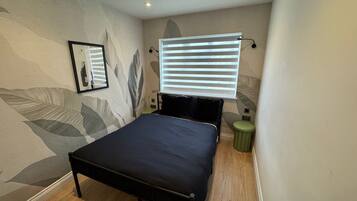 A bedroom with a bed, a wall-mounted light, a framed picture, and a window with blinds.