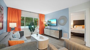 Una sala de estar moderna con sofá, sillones, una mesa de centro, televisor y una cama al fondo.